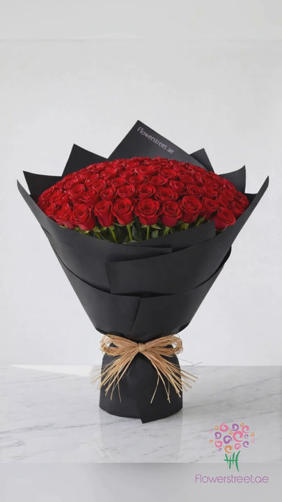 Dome bouquet of 101 red roses in black wrapping on marble, filmed in warm daylight as rose petals fall past