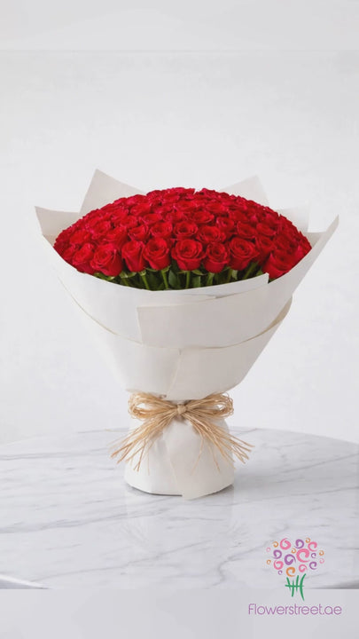 Dome bouquet of 101 red roses in white wrapping on marble, filmed in warm daylight as rose petals fall past