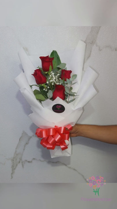 Four red roses with baby's breath and eucalyptus in white wrapping