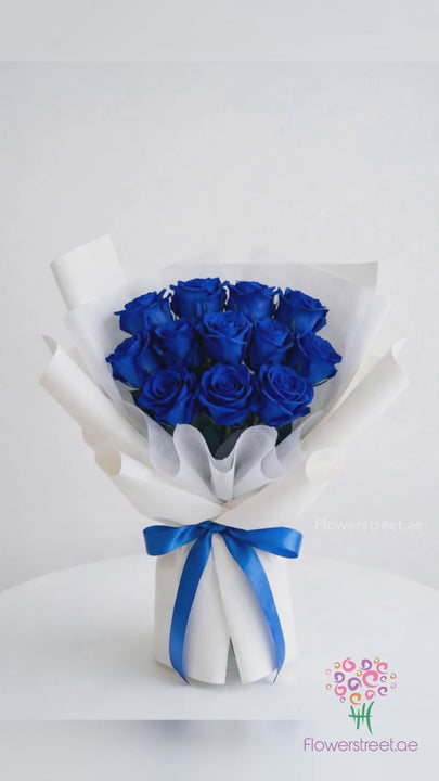 Grand royal blue rose bouquet in blue and white wrapping, filmed in warm light as petals fall past