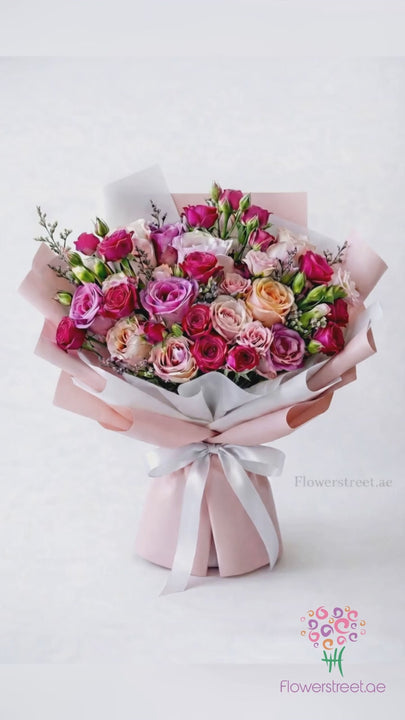 Blush pink and peach spray rose bouquet in pink wrapping, filmed in warm light as petals fall past