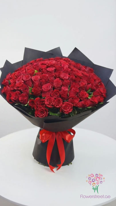 One hundred and one red roses in black and red wrapping, filmed in bright daylight as rose petals fall past