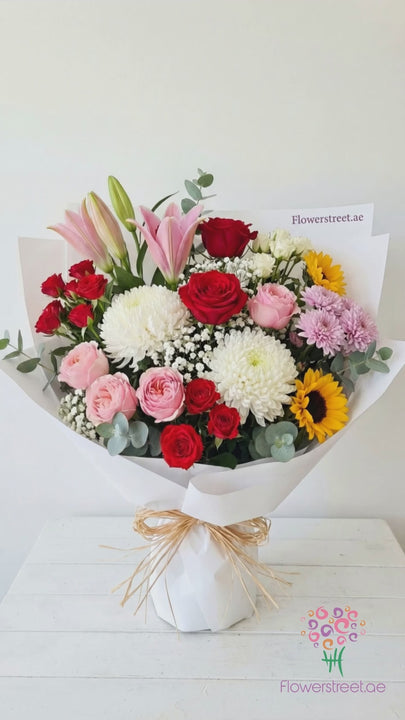 Colourful garden bouquet of pink lilies, roses, chrysanthemums and a sunflower, filmed in warm daylight as petals fall past