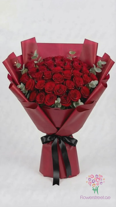 Forty red roses with eucalyptus in burgundy wrapping, filmed in warm light as rose petals fall past