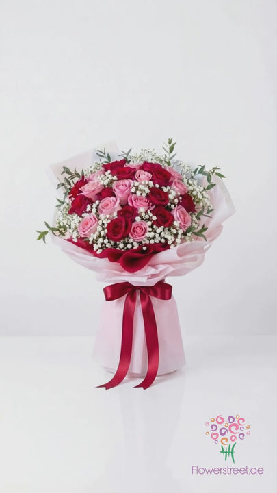 Grand bouquet of red and pink roses with baby's breath, filmed in warm light as petals fall past