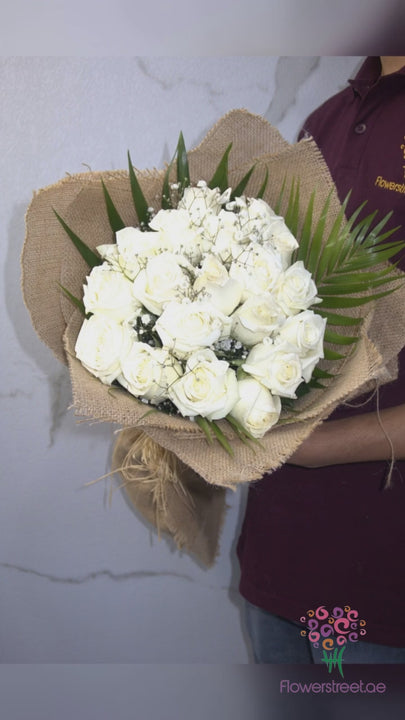 White roses with baby's breath and palm leaves in jute wrapping