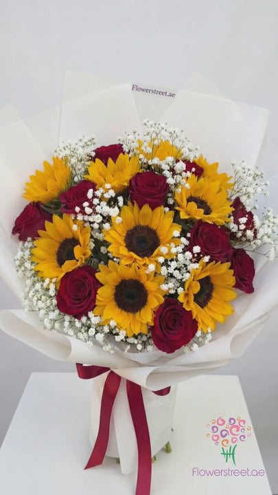 Bouquet of sunflowers and red roses with baby's breath in white wrapping, filmed in warm daylight as petals fall past