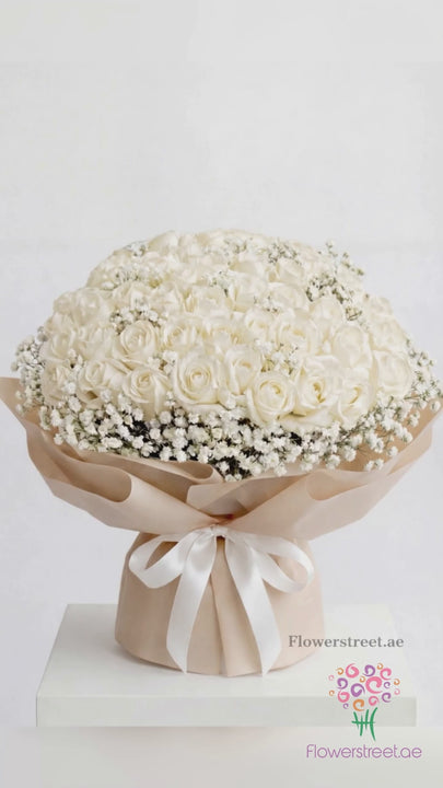 Dome bouquet of white roses with baby's breath in cream wrapping, filmed in soft daylight as white petals fall past