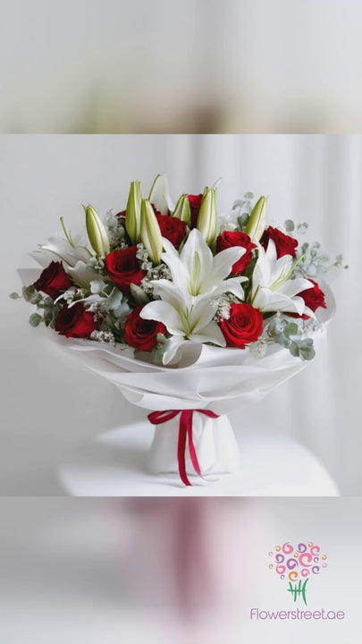 White lilies and red roses with baby's breath in white wrapping, filmed in soft daylight as rose petals fall past