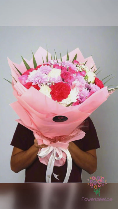 Mixed bouquet of pink, white and fuchsia flowers in pink and white wrapping, filmed in bright daylight as petals fall past