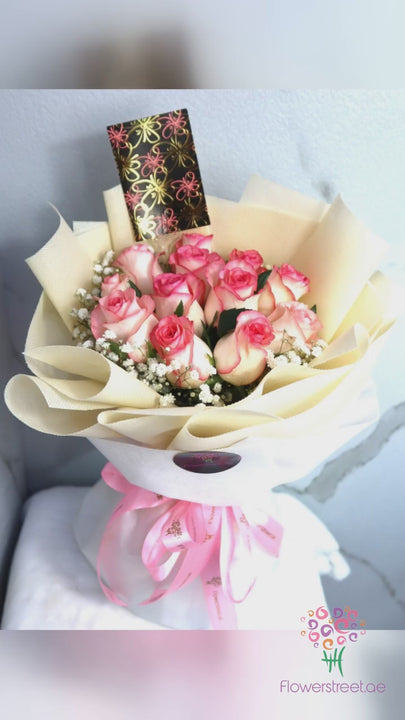 Twelve two-tone pink roses in cream and pink double wrapping, filmed in bright daylight as petals fall past