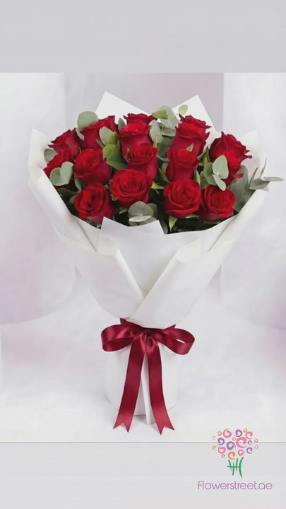 Red roses with eucalyptus in white wrapping, filmed in warm light as rose petals fall past