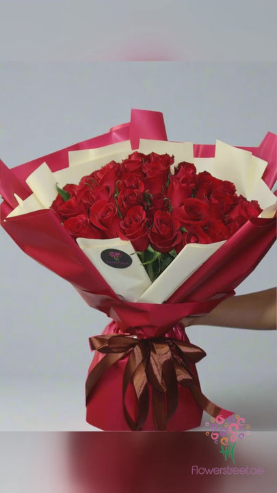 Fifty-one red roses in burgundy and cream double wrapping, filmed in bright daylight as rose petals fall past