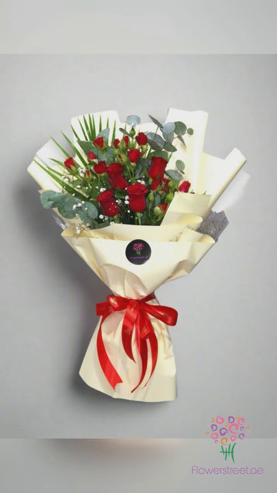 Red spray roses with green foliage in white wrapping, filmed in bright daylight as petals fall past