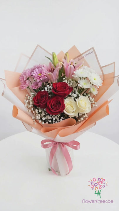 Pastel bouquet of pink lilies, roses and chrysanthemums in peach wrapping, filmed in warm light as petals fall past