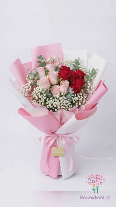 Dozen red and peach roses with baby's breath in pink wrapping, filmed in warm light as petals fall past