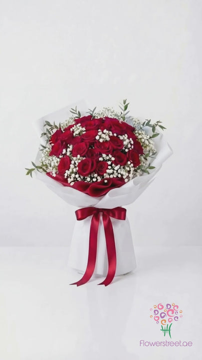 Grand bouquet of red roses with baby's breath in white wrapping, filmed in warm light as rose petals fall past